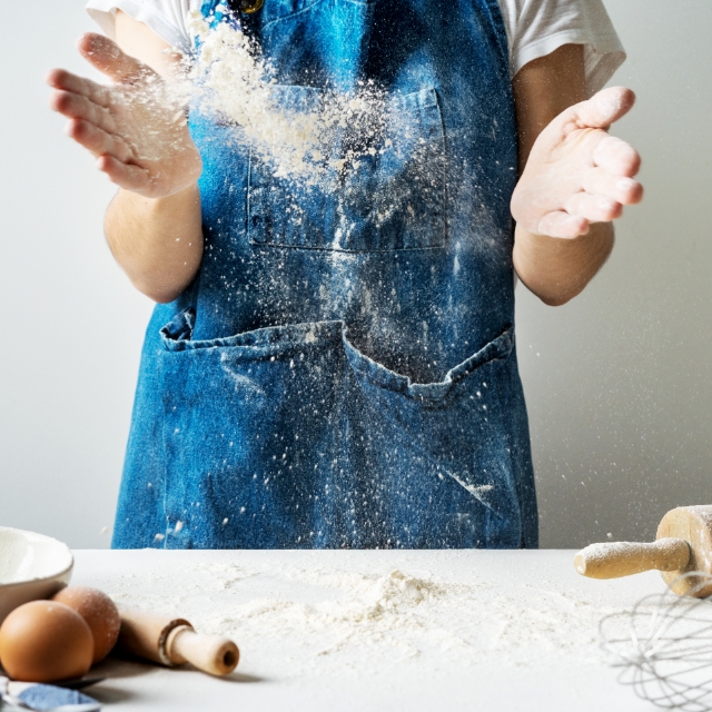 Human in an apron cooking with flour, eggs and a rolling pin