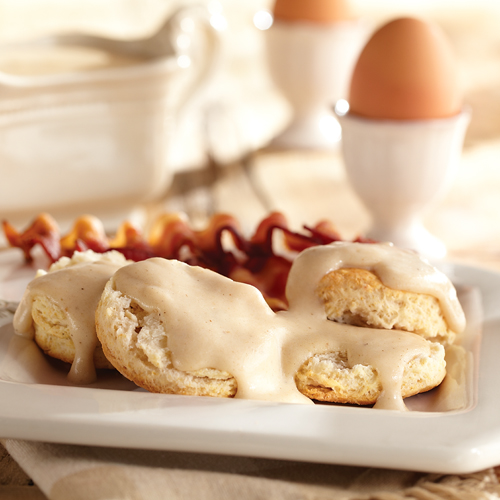 Fluffy biscuits with gravy covered on top, paired with bacon on the side